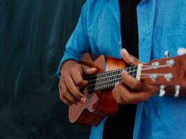 Indien Jeune homme dans une bleu chemise et des lunettes en jouant le guitare dans de face de le école tableau noir photo