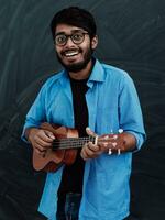 Indien Jeune homme dans une bleu chemise et des lunettes en jouant le guitare dans de face de le école tableau noir photo