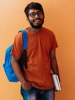 Indien étudiant avec bleu sac à dos, des lunettes et carnet posant sur Orange Contexte. le concept de éducation et scolarité. temps à aller retour à école photo