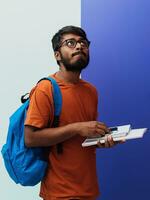 Indien étudiant avec bleu sac à dos, des lunettes et carnet posant sur le gris-violet Contexte. le concept de éducation et scolarité. temps à aller retour à école photo