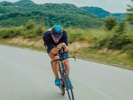 plein longueur portrait de un actif triathlète dans tenue de sport et avec une protecteur casque équitation une vélo. sélectif concentrer photo