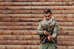 une soldat dans uniforme avec une fusil dans le sien main est permanent dans de face de une en bois mur. une soldat gardes le forêt base de le ennemi photo