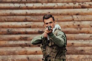 une soldat dans uniforme avec une fusil dans le sien main est permanent dans de face de une en bois mur. une soldat gardes le forêt base de le ennemi photo