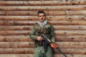 une soldat dans uniforme avec une fusil dans le sien main est permanent dans de face de une en bois mur. une soldat gardes le forêt base de le ennemi photo