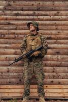 une soldat dans uniforme avec une fusil dans le sien main est permanent dans de face de une en bois mur. une soldat gardes le forêt base de le ennemi photo