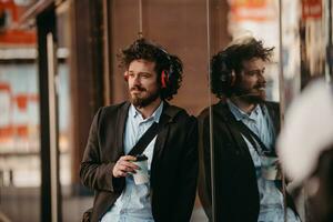 homme d'affaires à la mode avec une mallette en cuir dans le quartier financier à l'aide d'un smartphone tout en écoutant des chansons audio écouteurs buvant du café photo