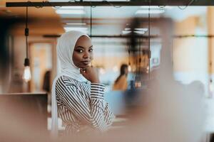 portrait de une noir Afro-américain femelle musulman permanent dans une moderne affaires Bureau tandis que portant une hijab. photo