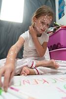 peu école fille avec varicelle dessin sur blanc planche dans enfants' chambre, antiseptique crème appliqué à visage et corps. tableau noir et jouets Contexte. photo