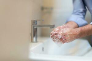 homme en utilisant savon et la lessive mains en dessous de le l'eau robinet. hygiène concept main fermer détail. photo