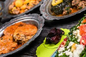 eid mubarak traditionnel Ramadan iftar dîner. assorti savoureux nourriture dans authentique rustique vaisselle sur en bois bleu Contexte. turc bosniaque nourriture Viande kebab, Pita, sarma, klepe, sogan dolma. photo