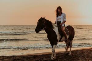 femme en vêtements d'été aime monter à cheval sur une belle plage de sable au coucher du soleil. mise au point sélective photo