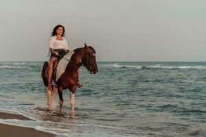 femme en vêtements d'été aime monter à cheval sur une belle plage de sable au coucher du soleil. mise au point sélective photo