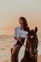 femme en vêtements d'été aime monter à cheval sur une belle plage de sable au coucher du soleil. mise au point sélective photo