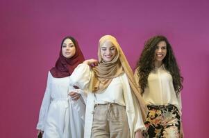 Trois musulman femmes dans hijab dans une moderne vêtements pose contre une rose Contexte photo