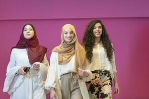 Trois musulman femmes dans hijab dans une moderne vêtements pose contre une rose Contexte photo