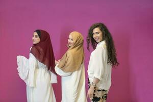 Trois musulman femmes dans hijab dans une moderne vêtements pose contre une rose Contexte photo