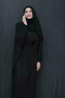 Jeune moderne musulman affaires femme en utilisant téléphone intelligent portant hijab vêtements dans de face de noir tableau noir photo