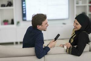 Jeune musulman couple femme portant islamique hijab vêtements séance sur canapé en train de regarder la télé ensemble pendant le mois de Ramadan à moderne Accueil photo