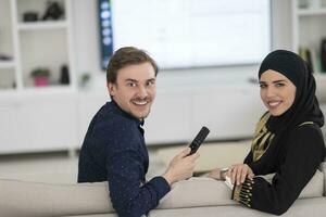 Jeune musulman couple femme portant islamique hijab vêtements séance sur canapé en train de regarder la télé ensemble pendant le mois de Ramadan à moderne Accueil photo