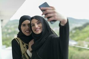 Jeune magnifique musulman femmes dans à la mode robe avec hijab en utilisant mobile téléphone tandis que prise selfie image sur le balcon représentant moderne Islam mode La technologie et Ramadan kareem concept photo