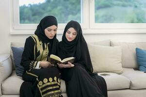 Jeune traditionnel musulman femmes lis coran sur le canapé avant iftar dîner pendant une Ramadan le banquet à maison. photo