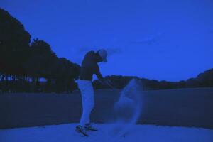 golfeur frappant un bunker de sable tourné au coucher du soleil photo