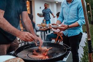 une groupe de copains et famille barbecue ensemble dans le soir sur le terrasse dans de face de une grand moderne maison photo