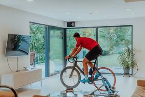 une homme équitation une triathlon bicyclette sur une machine simulation dans une moderne vivant chambre. formation pendant pandémie conditions. photo