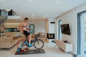 une homme équitation une triathlon bicyclette sur une machine simulation dans une moderne vivant chambre. formation pendant pandémie conditions. photo