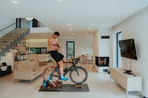 une homme équitation une triathlon bicyclette sur une machine simulation dans une moderne vivant chambre. formation pendant pandémie conditions. photo