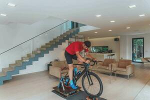 une homme équitation une triathlon bicyclette sur une machine simulation dans une moderne vivant chambre. formation pendant pandémie conditions. photo