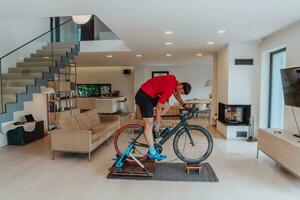 une homme équitation une triathlon bicyclette sur une machine simulation dans une moderne vivant chambre. formation pendant pandémie conditions. photo