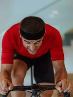 une homme équitation une triathlon bicyclette sur une machine simulation dans une moderne vivant chambre. formation pendant pandémie conditions. photo