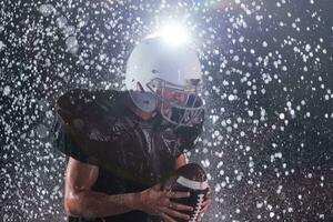 américain Football champ solitaire athlète guerrier permanent sur une champ détient le sien casque et prêt à jouer. joueur en train de préparer à courir, attaque et But atterrissage. pluvieux nuit avec spectaculaire brouillard, bleu lumière photo