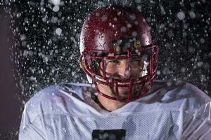 américain Football champ solitaire athlète guerrier permanent sur une champ détient le sien casque et prêt à jouer. joueur en train de préparer à courir, attaque et But atterrissage. pluvieux nuit avec spectaculaire brouillard, bleu lumière photo