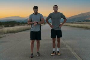 sport couple à la recherche à une montre intelligente tandis que permanent sur le pays route. repos après le jogging et fonctionnement exercice et vérification cœur taux et impulsion. photo