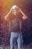 américain Football champ solitaire athlète guerrier permanent sur une champ détient le sien casque et prêt à jouer. joueur en train de préparer à courir, attaque et But atterrissage. pluvieux nuit avec spectaculaire brouillard, bleu lumière photo