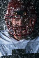 américain Football champ solitaire athlète guerrier permanent sur une champ détient le sien casque et prêt à jouer. joueur en train de préparer à courir, attaque et But atterrissage. pluvieux nuit avec spectaculaire brouillard, bleu lumière photo