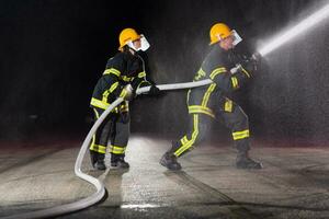 sapeurs pompiers en utilisant une l'eau tuyau à éliminer une Feu danger. équipe de femelle et Masculin pompiers dans dangereux porter secours mission. photo