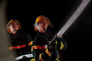 sapeurs pompiers utilisation une l'eau tuyau à éliminer une Feu danger. équipe de pompiers dans le dangereux porter secours mission. photo