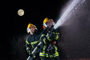 sapeurs pompiers en utilisant une l'eau tuyau à éliminer une Feu danger. équipe de femelle et Masculin pompiers dans dangereux porter secours mission. photo