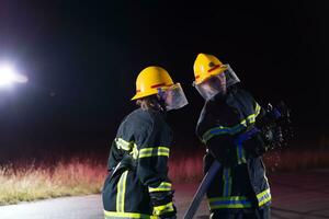 sapeurs pompiers en utilisant une l'eau tuyau à éliminer une Feu danger. équipe de femelle et Masculin pompiers dans dangereux porter secours mission. photo