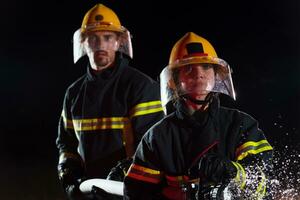 sapeurs pompiers en utilisant une l'eau tuyau à éliminer une Feu danger. équipe de femelle et Masculin pompiers dans dangereux porter secours mission. photo