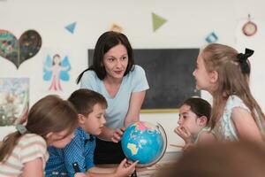 femelle prof avec des gamins dans la géographie classe à la recherche à globe. côté vue de groupe de diverse content école des gamins avec globe dans salle de cours à école. photo