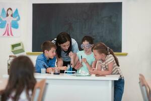 élémentaire école science salle de cours enthousiaste prof explique chimie à diverse groupe de enfants, peu garçon mélanges produits chimiques dans gobelets. les enfants apprendre avec l'intérêt photo