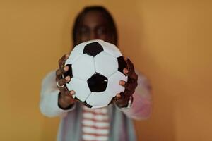 africain américain homme posant sur une Jaune Contexte tandis que en portant une football Balle photo