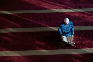 homme musulman priant allah seul à l'intérieur de la mosquée et lisant le livre de houx islamique photo