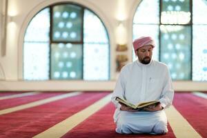 homme musulman priant allah seul à l'intérieur de la mosquée et lisant le livre de houx islamique photo