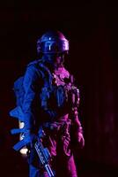 armée soldat dans combat uniformes avec un agression fusil et combat casque nuit mission foncé Contexte. bleu et violet gel lumière effet. photo