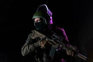 armée soldat dans combat uniformes avec un agression fusil et combat casque nuit mission foncé Contexte. bleu et violet gel lumière effet. photo